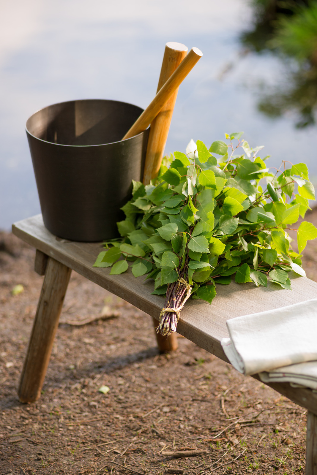 Birch whisk and other sauna objects on wooden bench by lake in Finland at midsummer.